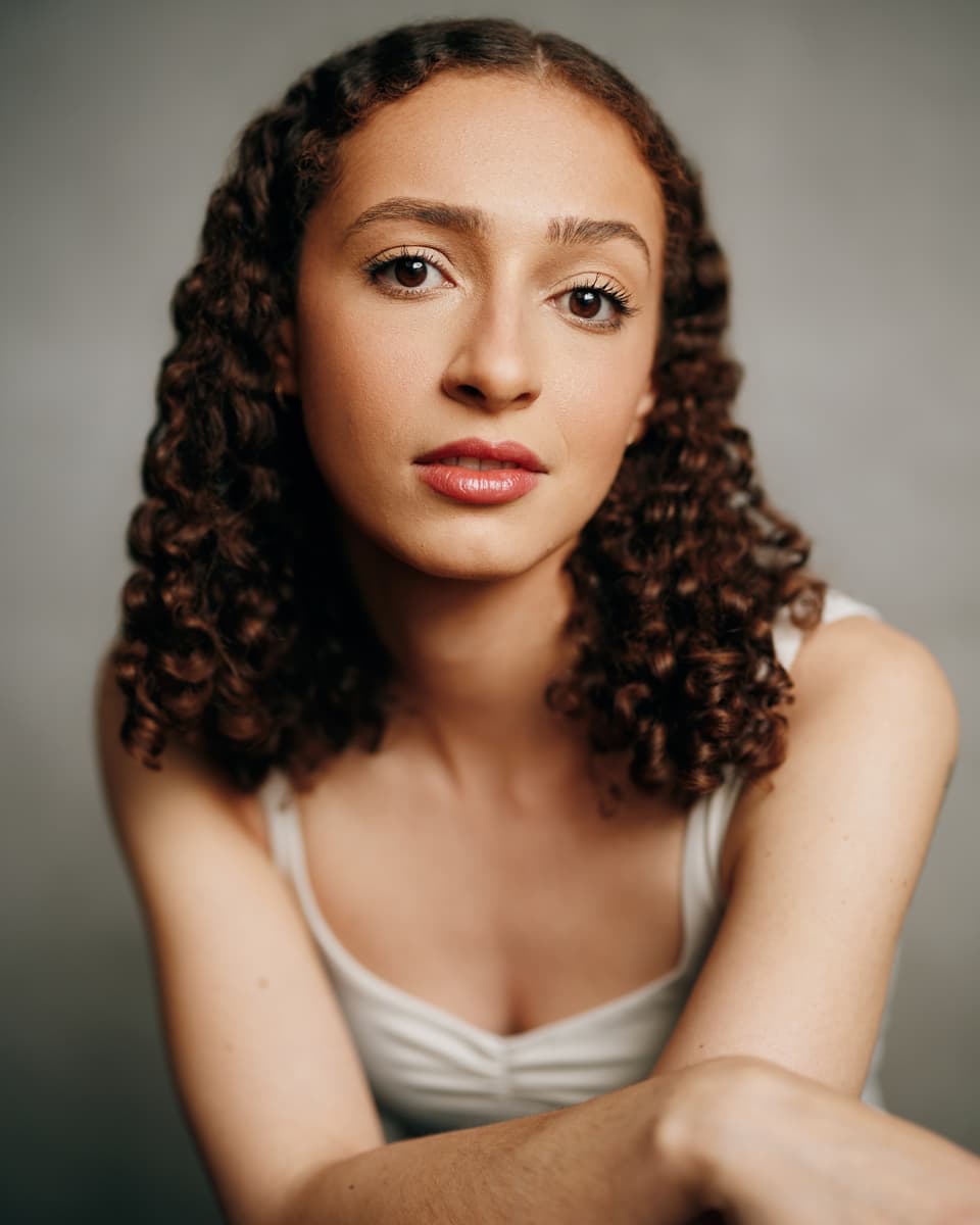 Actress headshot with a soft smile against a warm cream backdrop