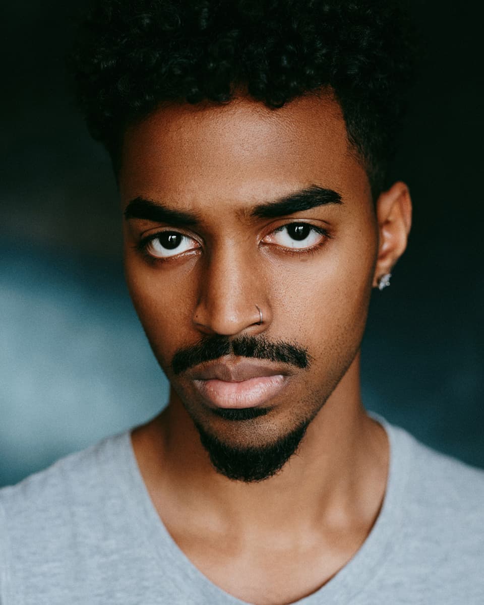 Toronto theatrical actor headshot of a man with arms crossed and an intense, commanding expression against a studio backdrop