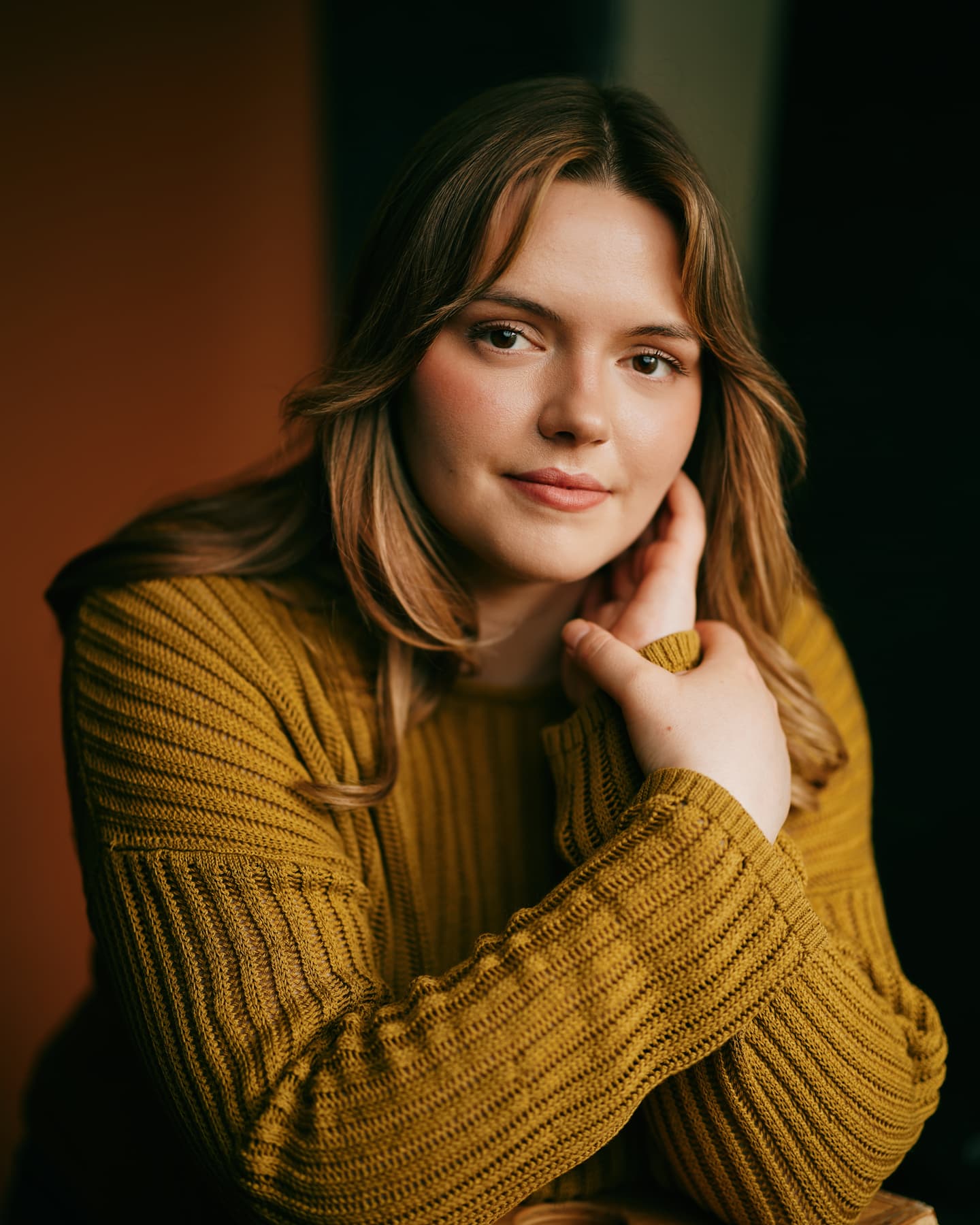 Toronto actor headshot of a young woman with long dark brown hair and green eyes, wearing a black V-neck top, gazing directly at the camera with a calm expression against a deep dark teal background